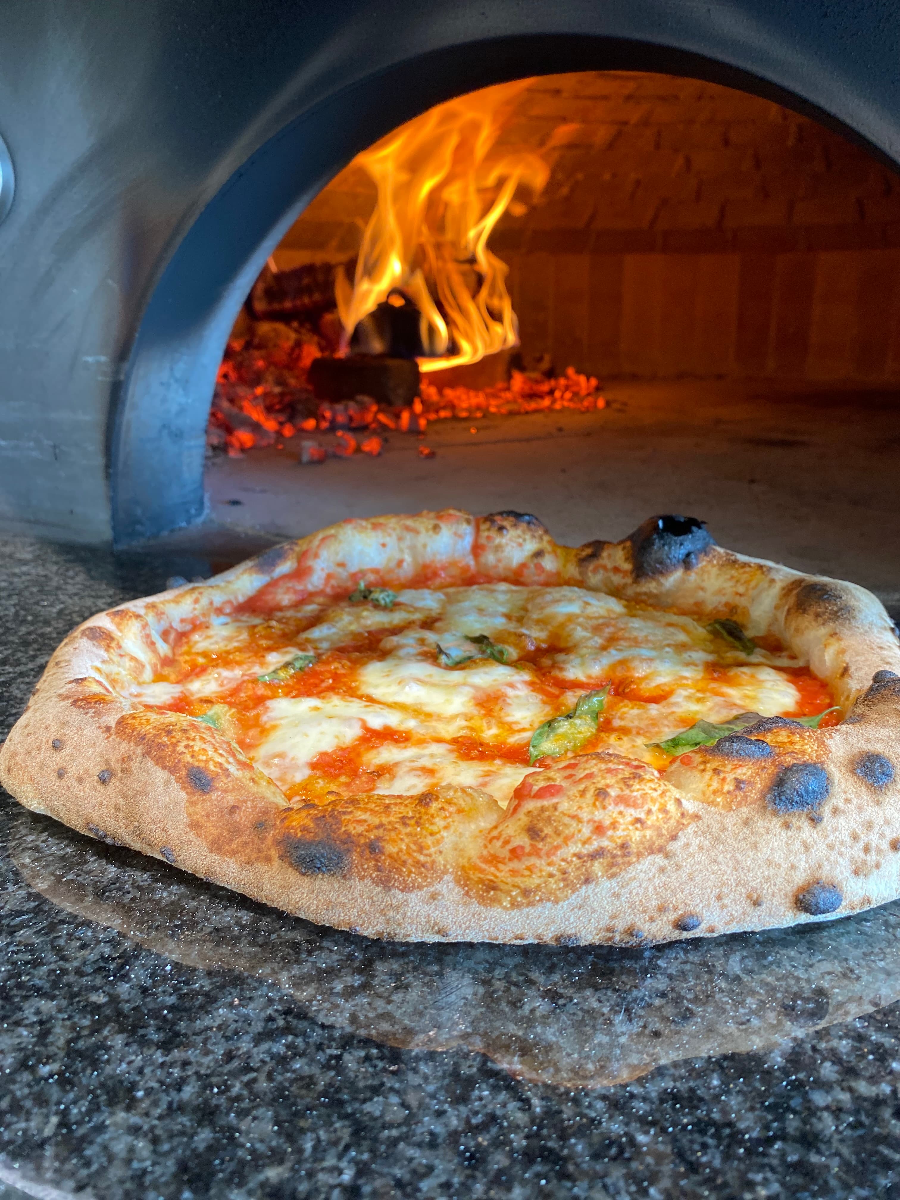 Pizza Margherita na blacie pieca, w tle płomienie